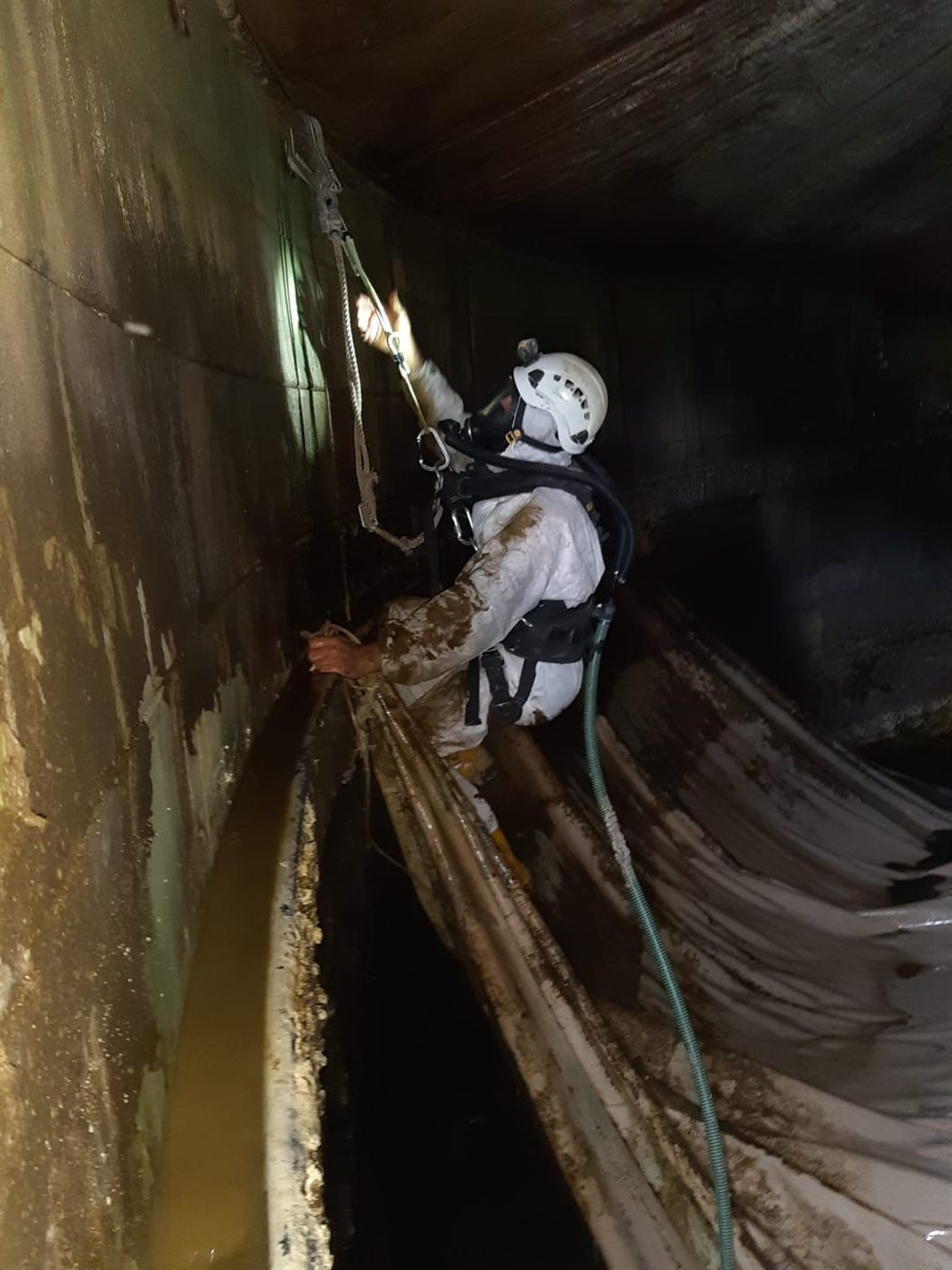 Tecnico con tuta, maschera e imbracatura dentro un digestore svuotato
