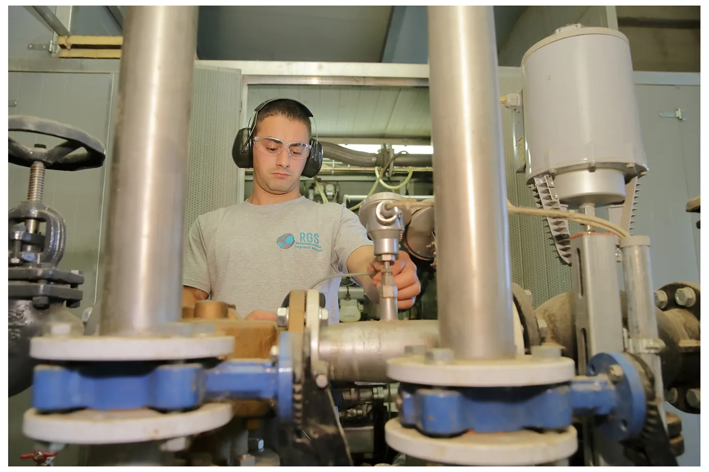 Tecnico RGS con le cuffie di protezione controlla la linea del gas del cogeneratore in un impianto biogas